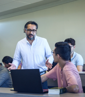 A teacher engaging with a student during a class session while other students work independently in the background, embodying the Neeyamo Foundation's mission to empower youth