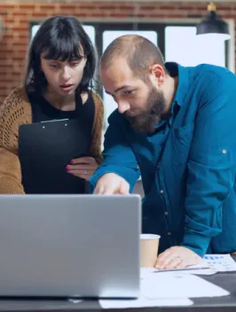 Two colleagues, a man and a woman, are focused on a laptop screen in an office setting both engaged in discussing global payroll.